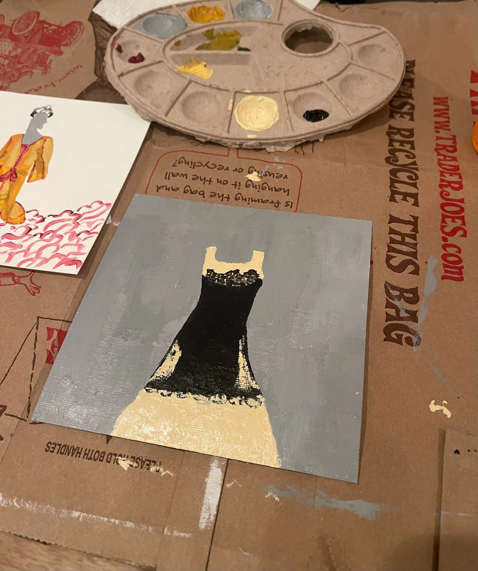 a just-finished painting of a black dress beside a paint palette
