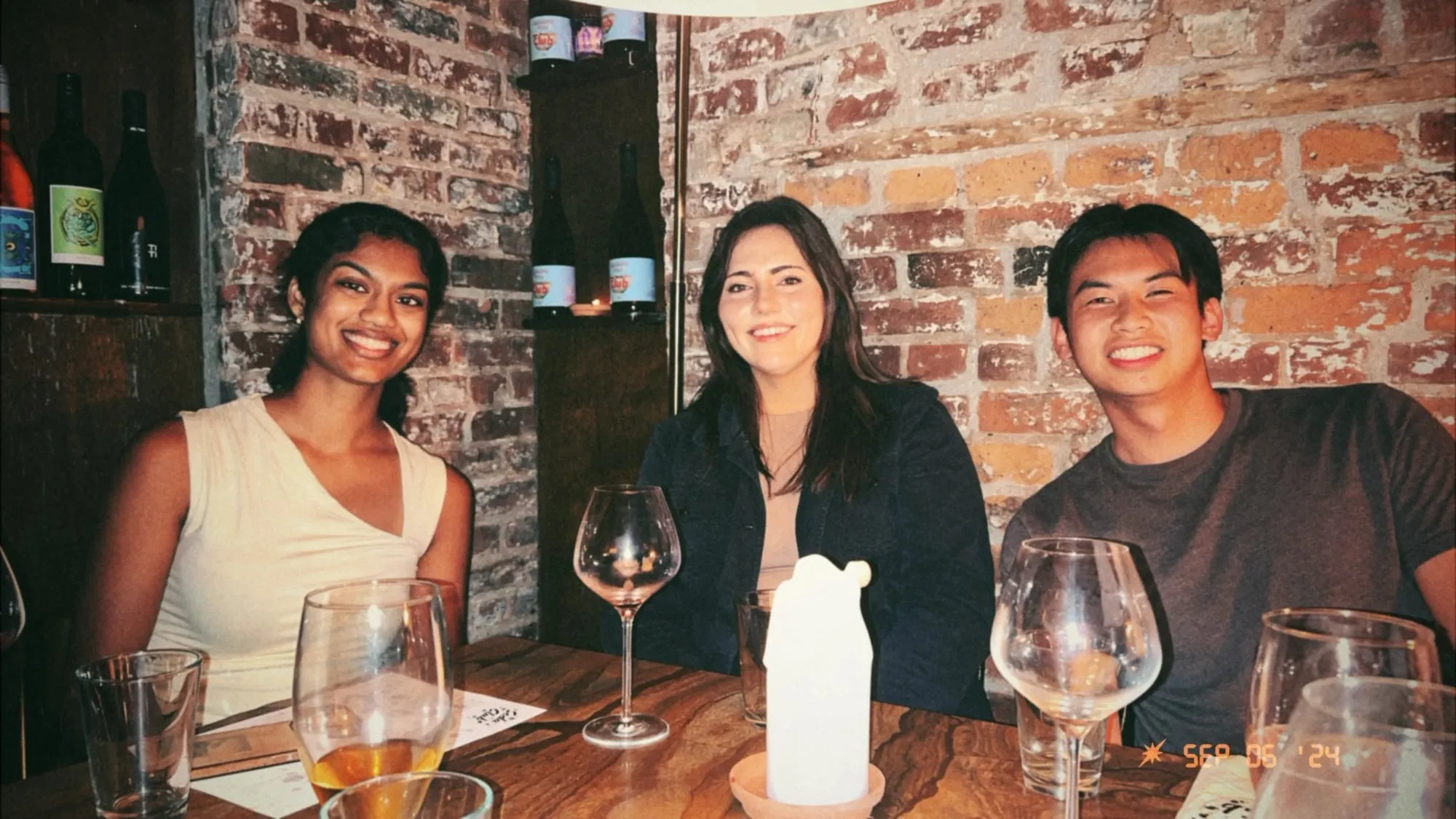 sahi and two friends smiling at a candlelit table against a brick wall